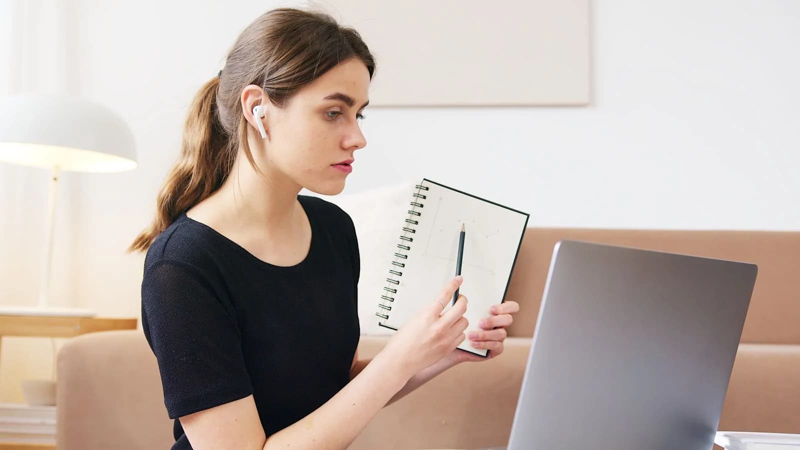 Student attending a live online lesson on a laptop, taking notes